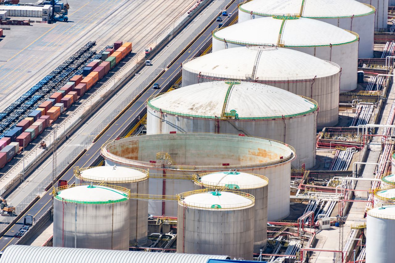 Aerial shot of large oil storage tanks in an industrial district with adjacent railway tracks.
